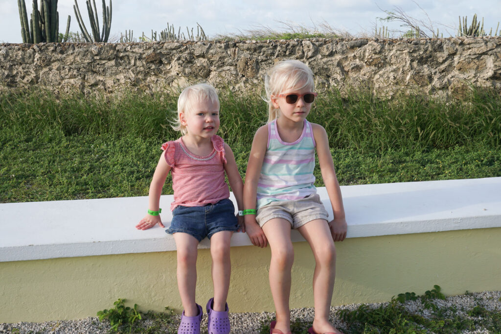 two young girls sitting on low wall in aruba